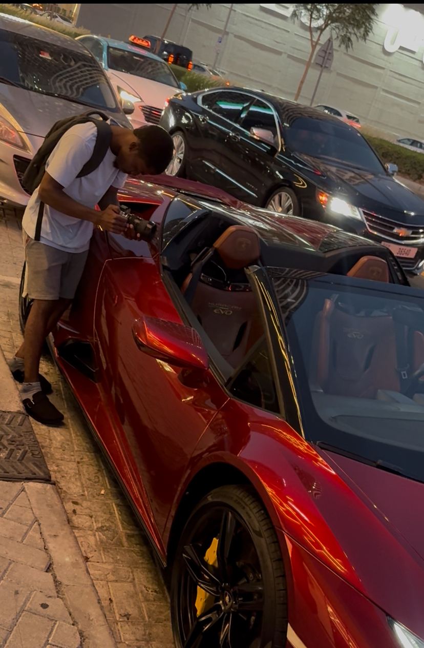 Chancio penché sur une supercar rouge décapotable, caméra en main