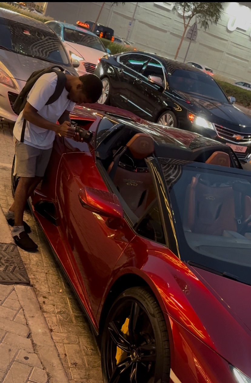 Chancio penché sur une supercar rouge décapotable, caméra en main