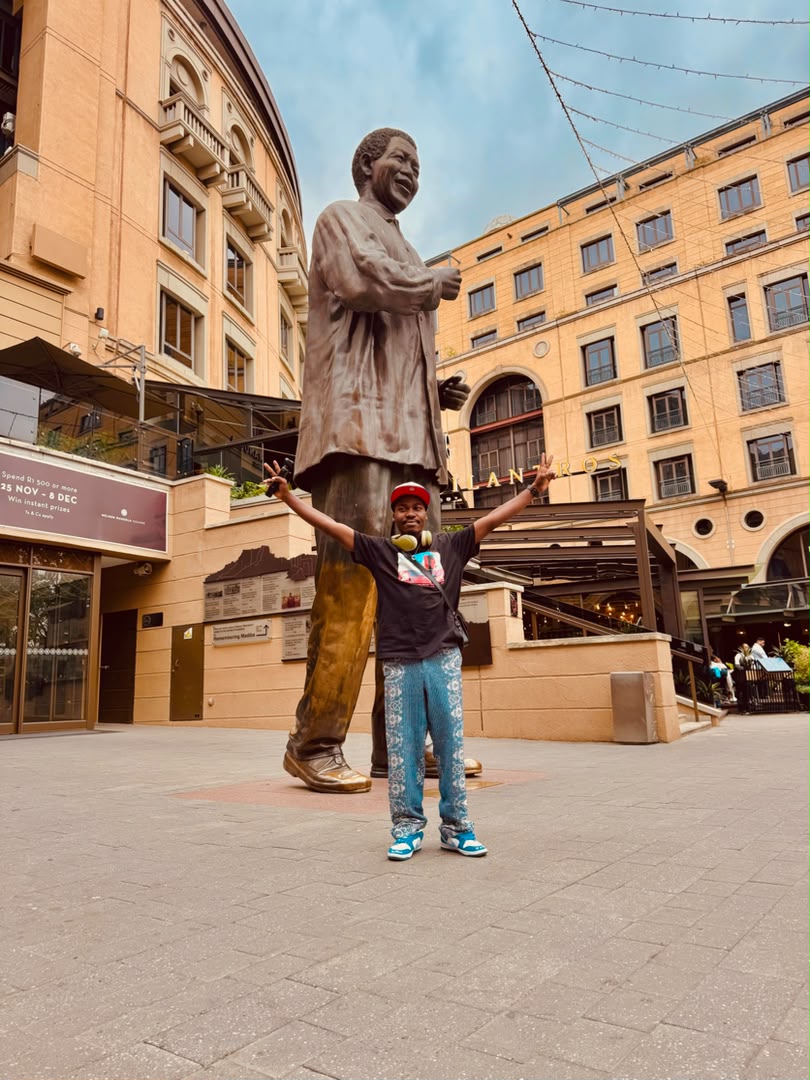 Chancio bras écartés devant la statue de Nelson Mandela, sur Nelson Mandela Square à Johannesburg