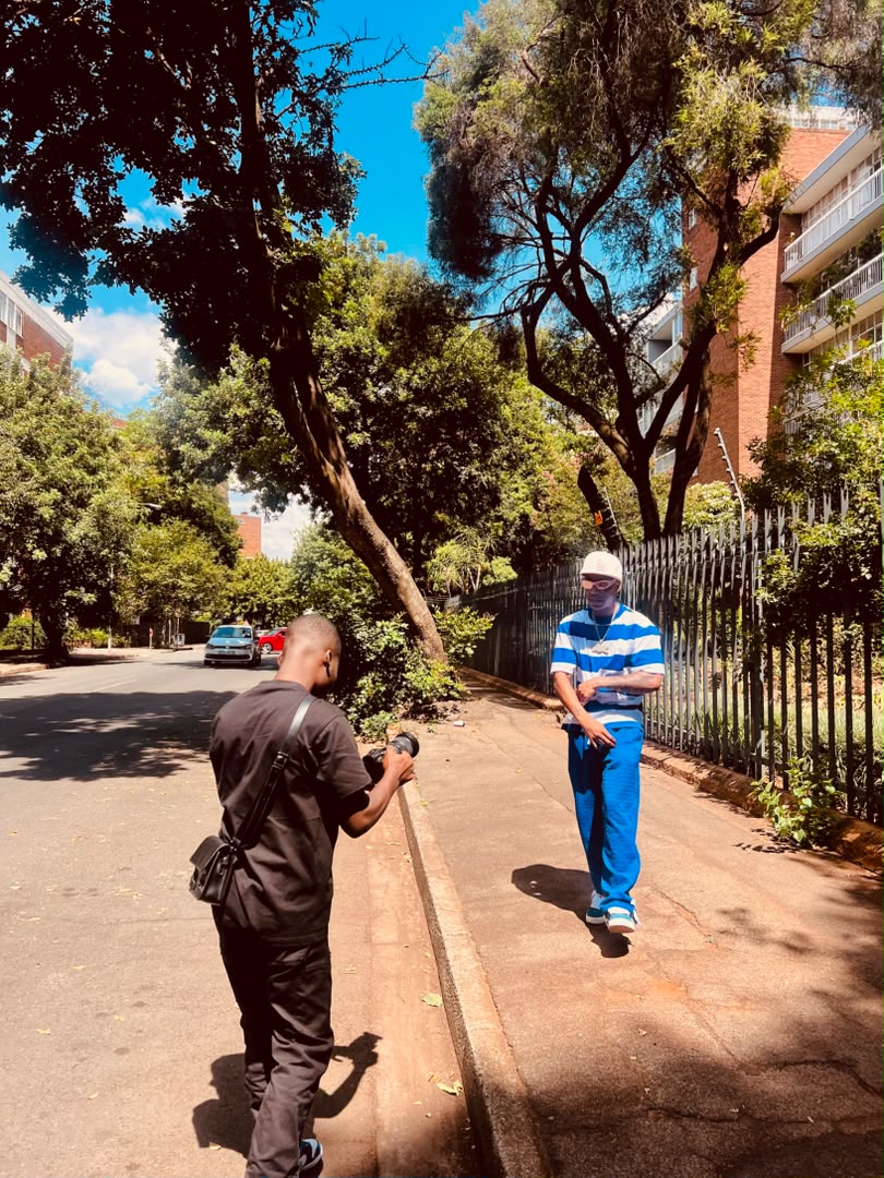 Chancio filmant un artiste qui marche sur un trottoir d’une rue arborée de Johannesburg